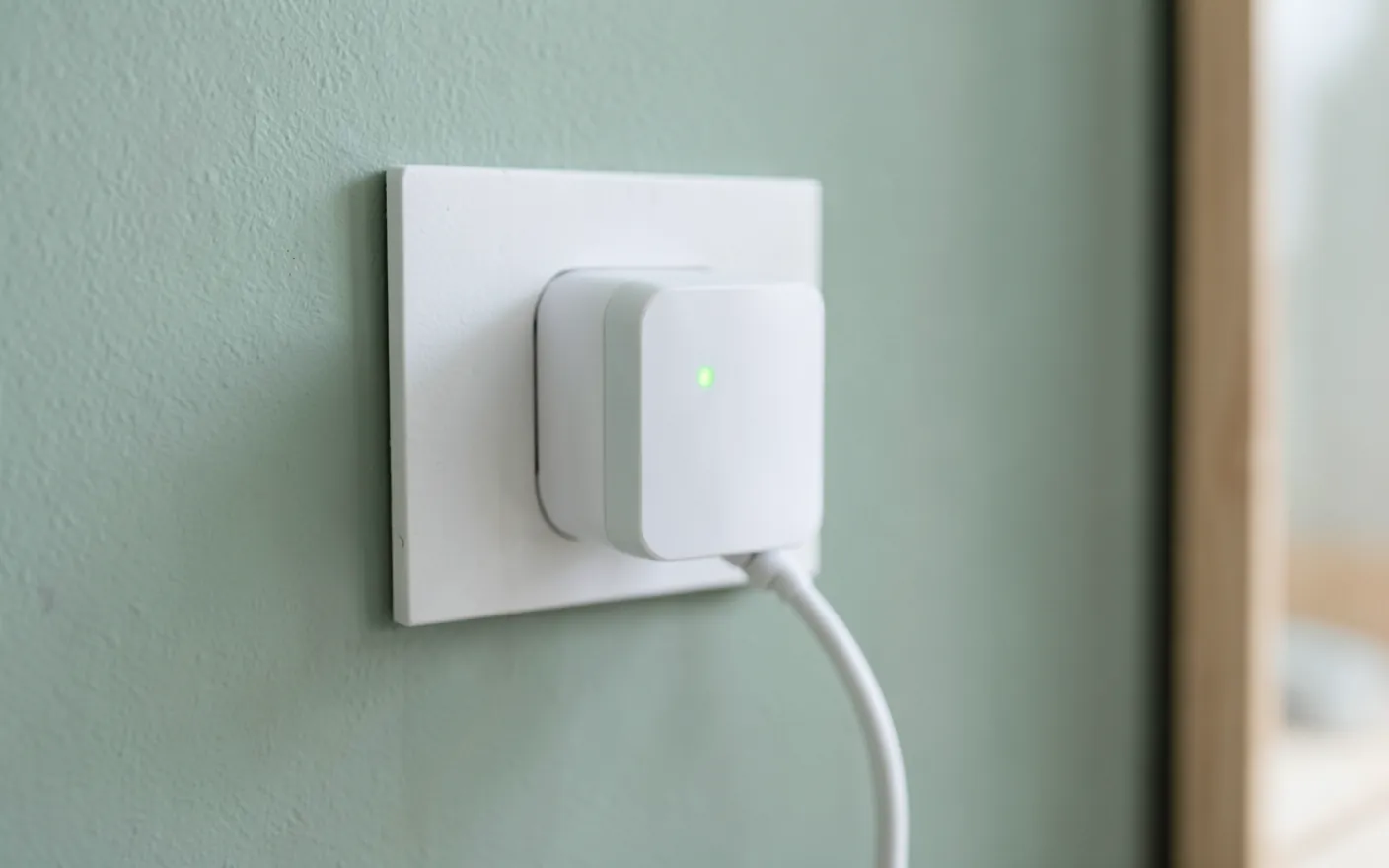 Enchufe inteligente blanco con una luz verde conectado a una pared verde salvia